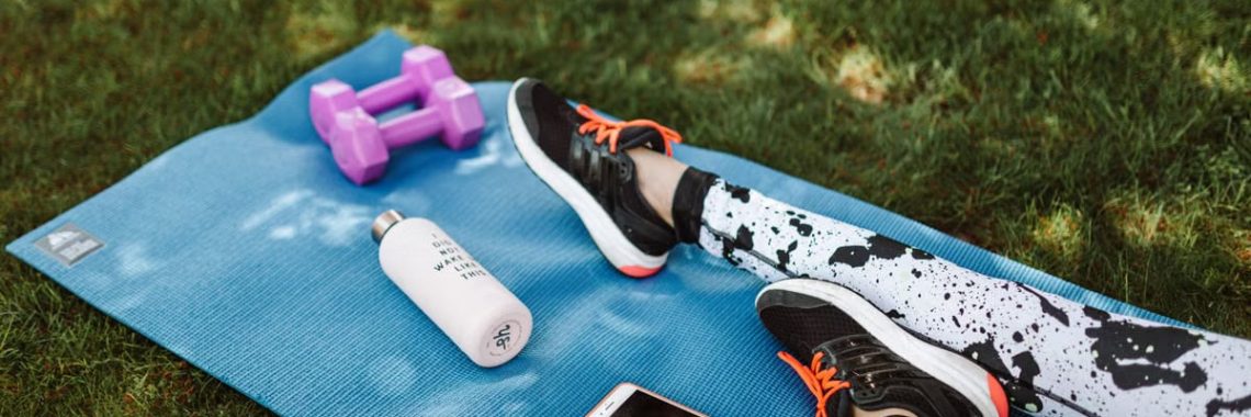 Focused workout setup outdoors with mat, dumbbells, phone, and water bottle.