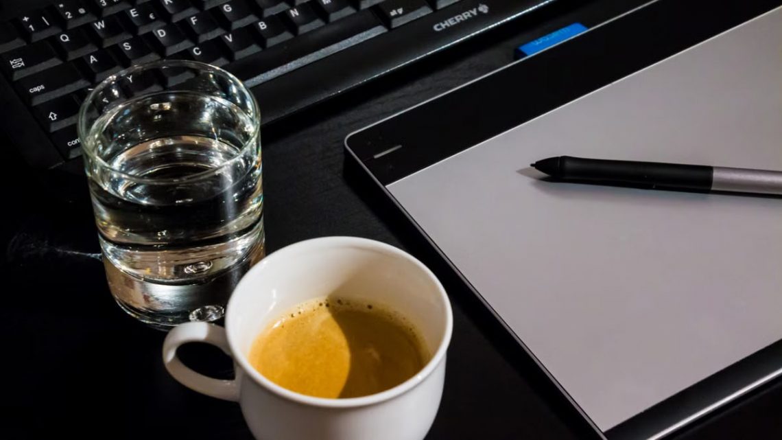 Office desk setup with a coffee cup, glass of water, tablet, pen, and keyboard.