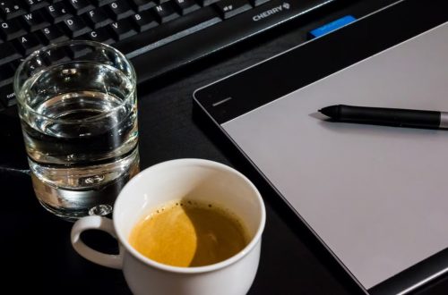 Office desk setup with a coffee cup, glass of water, tablet, pen, and keyboard.